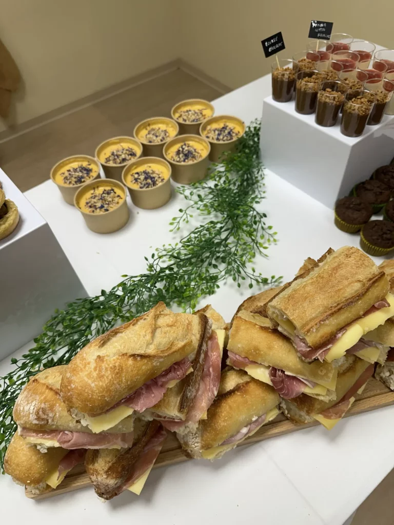 Buffet réalisé par Maison Mélia, avec sandwichs jambon-fromage, desserts en verrines et douceurs sucrées présenté sur table d’événement.