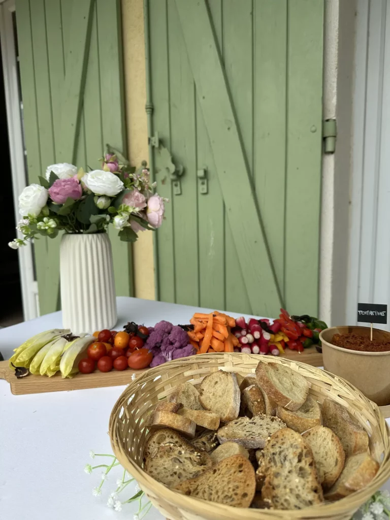 Buffet de légumes frais et pain en tranches présenté sur table avec un bouquet de fleurs, lors d’un événement en extérieur.