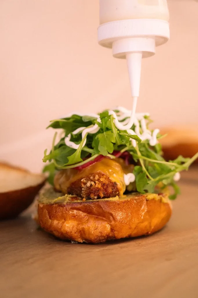 Assemblage d’un burger avec steak, roquette et sauce, dressé sur pain brioché.