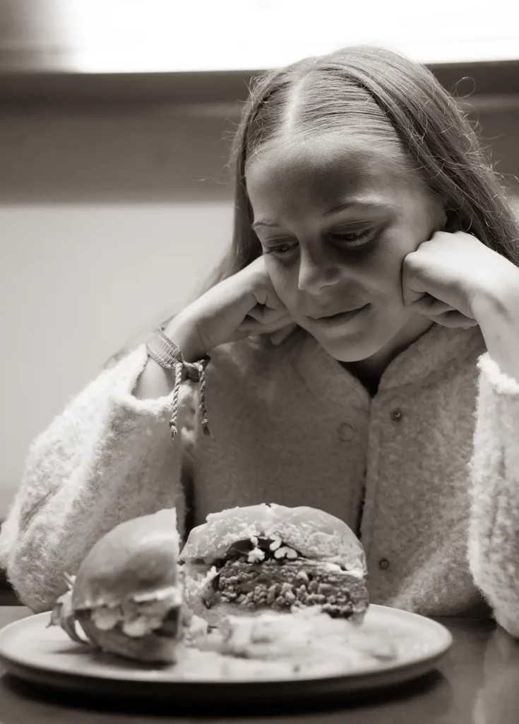 Enfant regardant un burger coupé en deux posé sur une assiette.