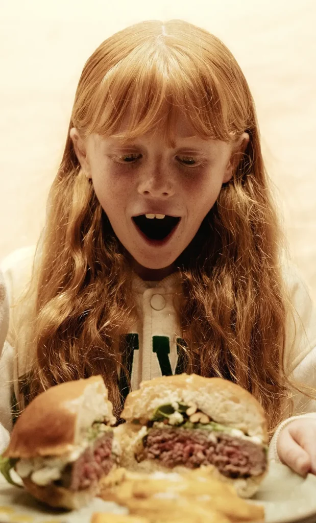 Enfant émerveillé découvrant un burger coupé en deux servi sur assiette.