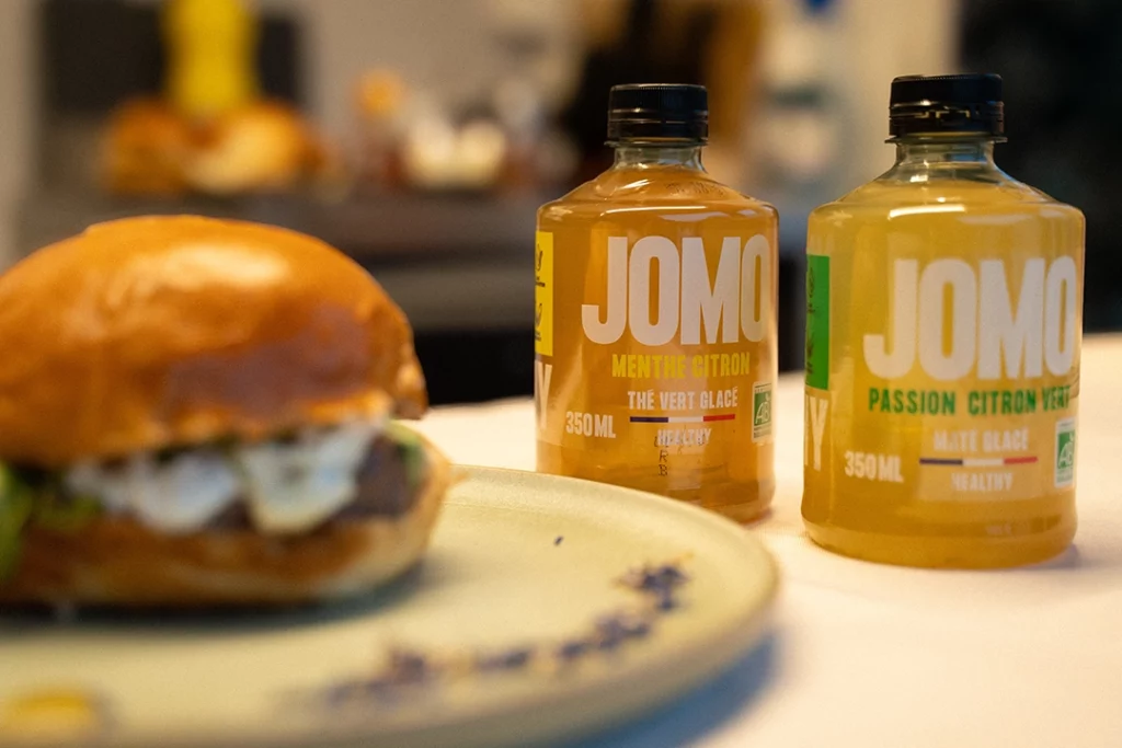 Bouteilles de thé glacé JOMO présentées avec un burger sur assiette.