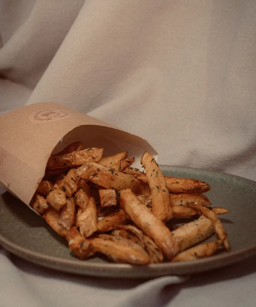 Frites fait maison servies dans un cornet en papier sur assiette.